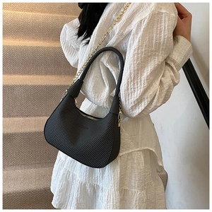 Detail of black woven shoulder bag with gold chain strap styled on a white dress