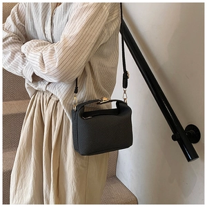 Detail of black textured crossbody bag with gold hardware worn by a model in a minimal setting