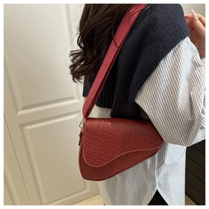 Detail of burgundy saddle bag with crocodile texture worn over shoulder by a model