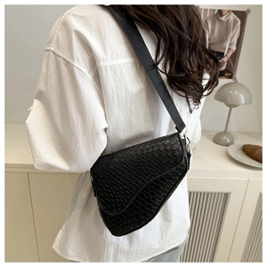 Close-up of black woven texture saddle bag with gold metal buckle and wide strap