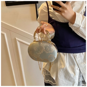 Detail of elegant chain evening bag with intricate gold floral embroidery and metal handle
