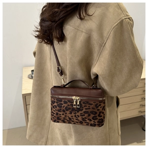 Détail du sac boîte léopard avec fermetures dorées porté sur un trench-coat en daim beige