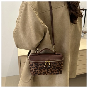 Détail du sac bandoulière léopard avec fermetures dorées porté sur un manteau camel