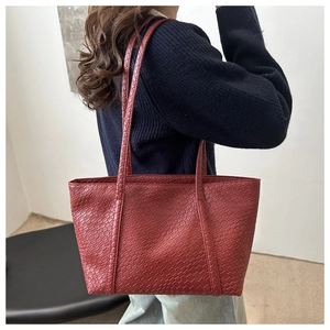 Detail of burgundy woven tote bag showing texture and shoulder straps on a model
