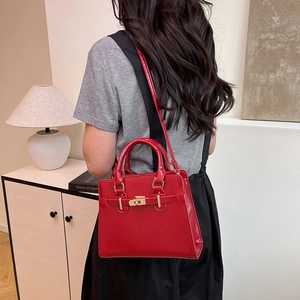 Minimalist red glossy shoulder bag with gold twist lock shown in a modern home interior