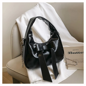 Close-up of black glossy patent leather shoulder bag with oversized bow and chain