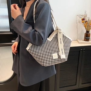 Chic houndstooth tote bag with white leather trim shown on shoulder in urban setting