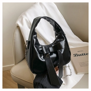 Detail of glossy black leather handbag with a large bow and silver chain strap
