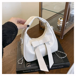 Detail of white hobo bag with large bow, glossy leather texture, and silver chain strap