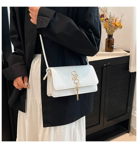 Detail of white crocodile pattern bag with gold S-shaped metal hardware and fringe