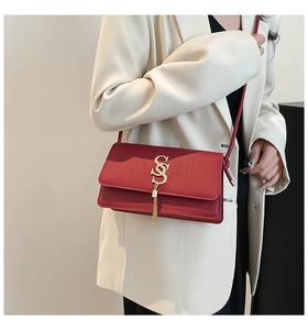 Detail of red crocodile texture handbag with gold SSS logo and metallic tassel pendant