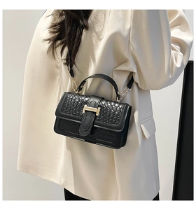 Close-up of black woven leather handbag featuring gold H-shaped buckle and metal hardware