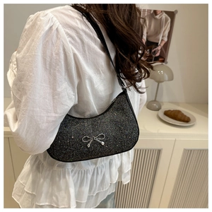 Detail of black sequin underarm bag with silver metal bow on a croissant bag model