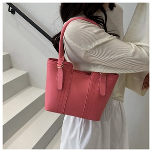 Detail of pink leather tote bag featuring decorative stitching and metal hardware on white stairs