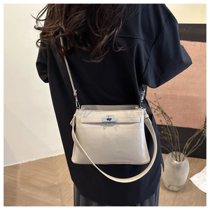 Cream-colored shoulder bag with silver turn-lock clasp worn by a model in a cozy room