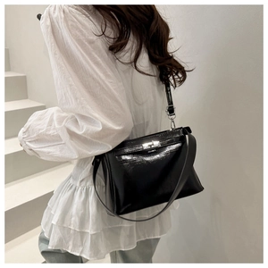 Detail of black glossy leather shoulder bag featuring a silver metal buckle and strap