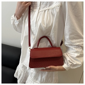 Detail of red crossbody bag showing textured snake pattern and golden hardware accents