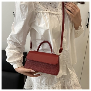Detail of red crossbody bag with crocodile texture and adjustable shoulder strap worn by model