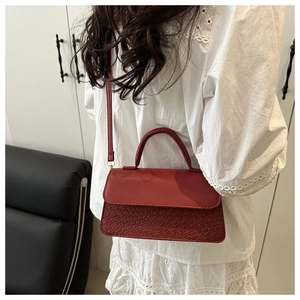 Detail view of red leather crossbody bag with snake-skin pattern and gold hardware