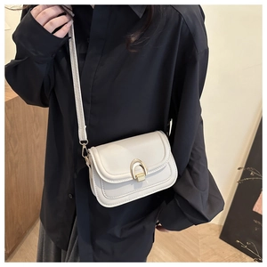 Detail of minimalist cream crossbody bag with gold U-shaped clasp on black shirt