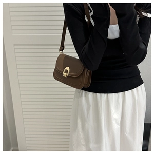 Detail of a brown leather crossbody bag with a golden horseshoe buckle on a model
