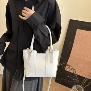 Minimalist white PU leather bucket handbag with round handles and gold hardware worn by a model
