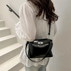 Classic black patent leather crossbody bag with silver buckle worn by a model in a modern setting
