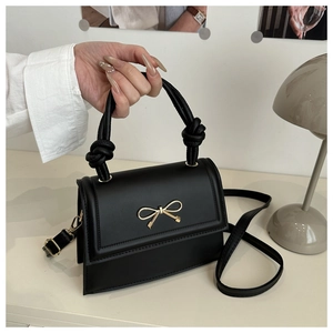 Détail du petit sac noir en cuir avec boucle nœud dorée et poignée à nœud élégante