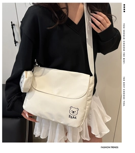 Detail view of white canvas messenger bag with bear graphic and round coin purse charm