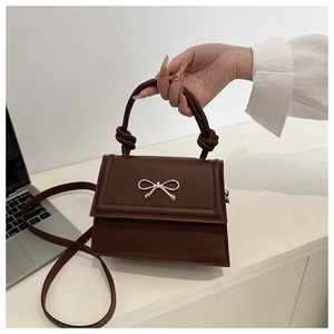 Détail d'un sac bandoulière marron avec fermoir nœud doré et poignée nouée