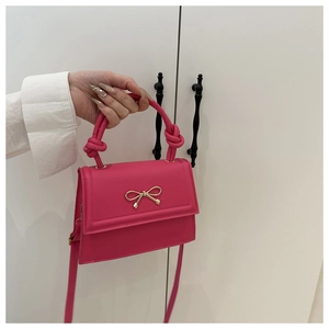 Détail du sac bandoulière fuchsia avec nœud doré et poignée nouée élégante