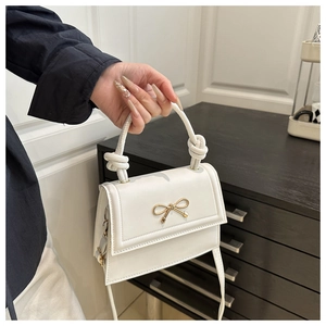 Détail d'un sac bandoulière blanc avec nœud doré et poignée nouée élégante