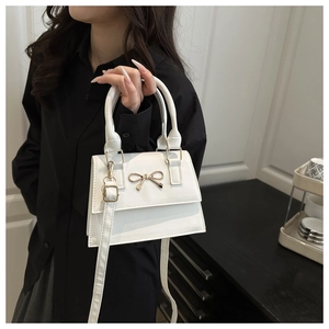 Detail of white crossbody bag with golden bow ornament and shiny leather texture
