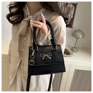 Detail of a black crossbody bag with golden bow hardware held by a model in soft light