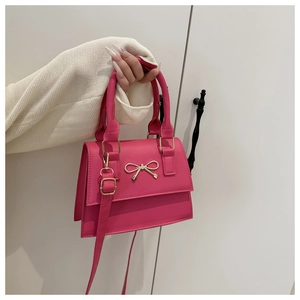 Close-up of bright pink shoulder bag featuring a decorative golden metal bow on the flap