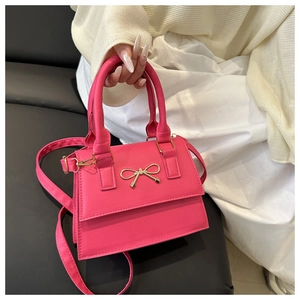 Detailed shot of hot pink leather bag featuring a gold metal bow and dual handles