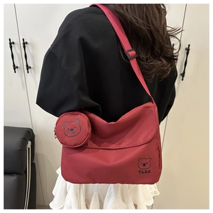 Detail view of burgundy nylon crossbody bag with small round coin pouch and bear graphic