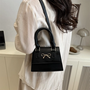 Classic black leather handbag with golden bow buckle shown in a modern lifestyle setting