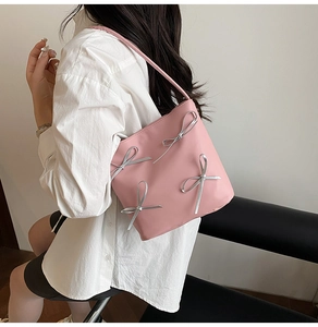 Detail view of a pink bucket bag with silver ribbon bows worn by a model in casual attire