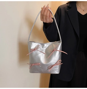 Detail of silver handbag featuring pink ribbon bows held by a model in a black suit