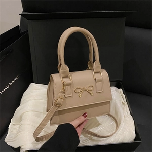 Beige faux leather handbag with gold bow hardware on silk lining inside a black gift box