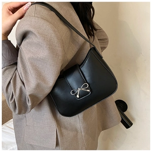 Close-up of black matte shoulder bag featuring a silver metal bow buckle on a flap cover