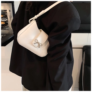 Detailed shot of white leather baguette bag with silver bow ornament on black blazer