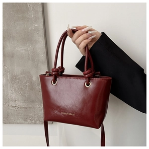 Dettaglio della mini borsa tote bordeaux con manici annodati e occhielli in metallo