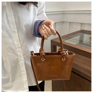 Dettaglio di una borsa a secchiello in pelle marrone con manico a nodo e scritte oro