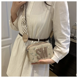 Dettaglio borsa a tracolla intrecciata beige con ricami floreali e logo SM in metallo
