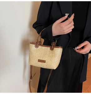 Dettaglio della borsa a secchiello in paglia con manici in pelle marrone indossata da una modella