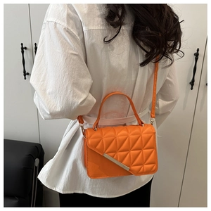Detail of bright orange quilted square crossbody bag with silver metal bar on a white shirt