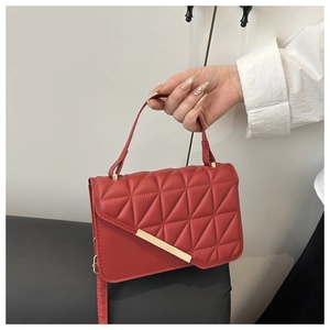 Close-up of red quilted crossbody bag with asymmetric flap and golden metal bar detail