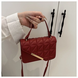 Detail of red quilted faux leather handbag with geometric patterns and gold metal bar